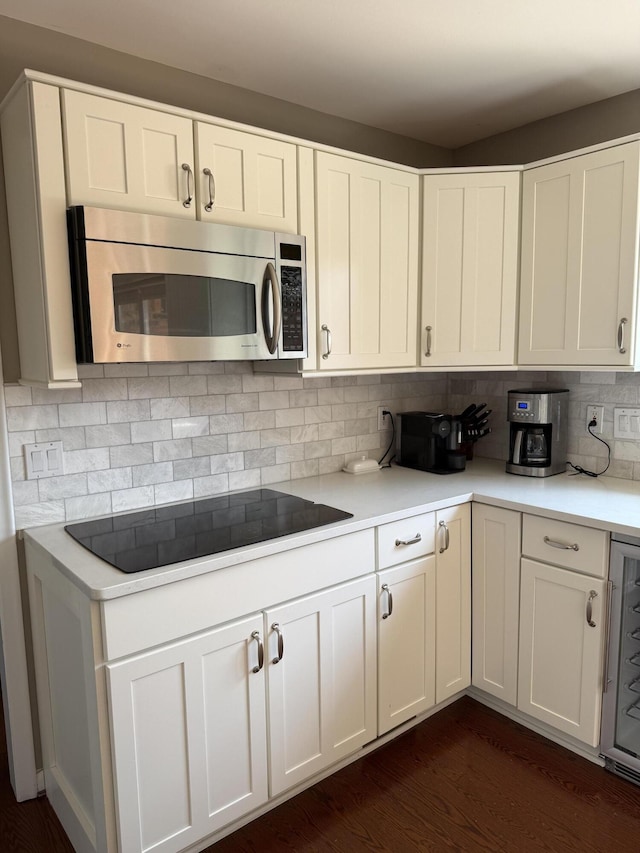 kitchen featuring black electric stovetop, light countertops, white cabinetry, stainless steel microwave, and backsplash