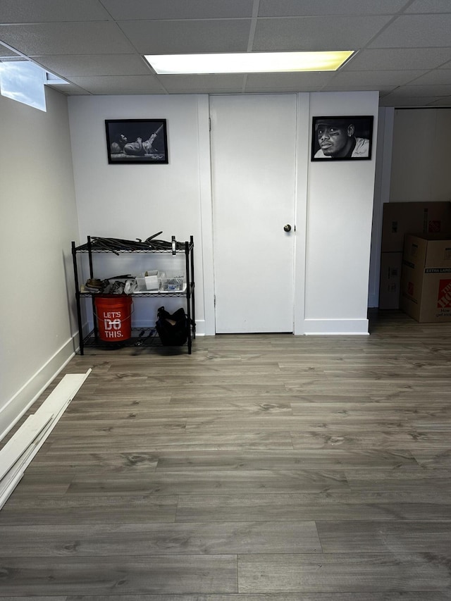 finished below grade area with baseboards, a drop ceiling, and wood finished floors