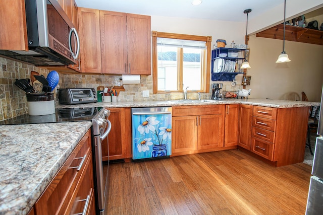 kitchen with appliances with stainless steel finishes, a sink, light wood-style floors, a peninsula, and backsplash