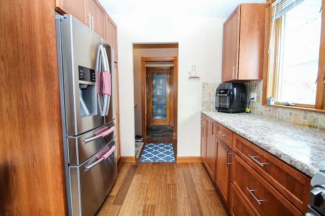 kitchen with brown cabinetry, tasteful backsplash, wood finished floors, baseboards, and stainless steel fridge