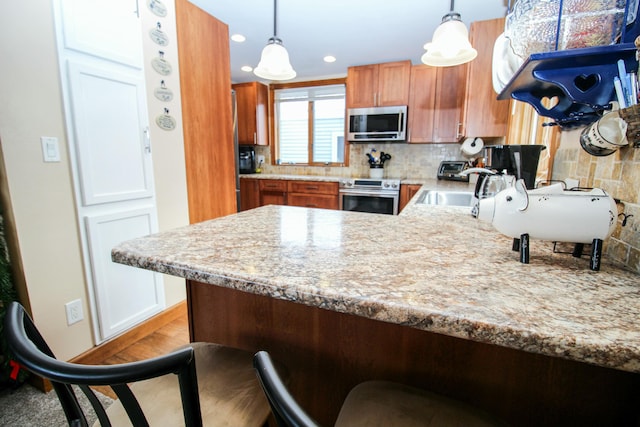 kitchen with decorative backsplash, hanging light fixtures, a sink, a peninsula, and stainless steel appliances
