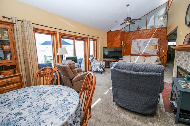 living area with a ceiling fan, a brick fireplace, carpet floors, high vaulted ceiling, and wooden walls