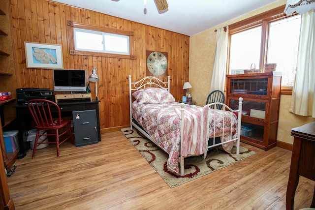 bedroom with ceiling fan, wood walls, and wood finished floors