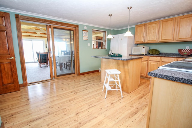 kitchen with a kitchen island, light brown cabinetry, dark countertops, white microwave, and light wood-style flooring