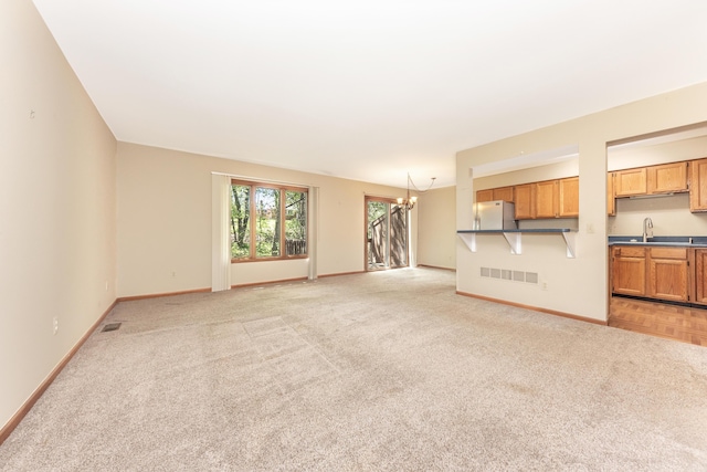 unfurnished living room featuring visible vents, light carpet, baseboards, a chandelier, and a sink
