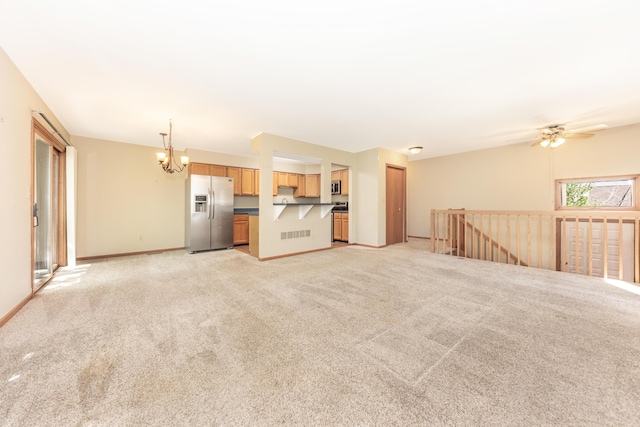 unfurnished living room with visible vents, baseboards, ceiling fan with notable chandelier, and light colored carpet