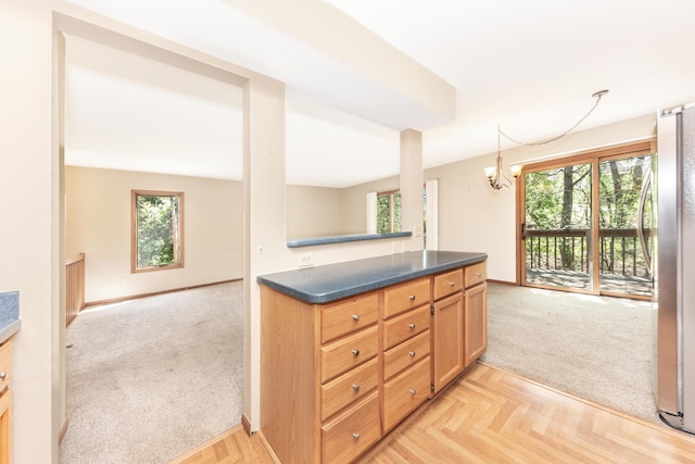 kitchen with dark countertops, freestanding refrigerator, a chandelier, and light carpet