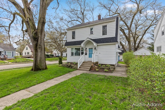 view of front of property with a shingled roof, a front lawn, and a chimney