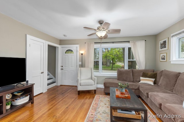 living room with stairway, baseboards, ceiling fan, and light wood finished floors