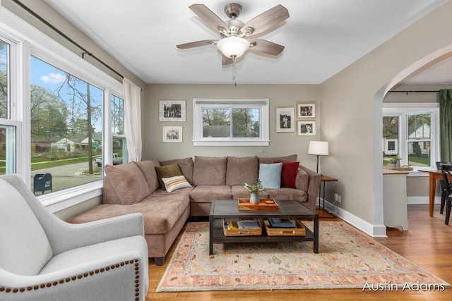 living area featuring baseboards, arched walkways, a ceiling fan, and wood finished floors