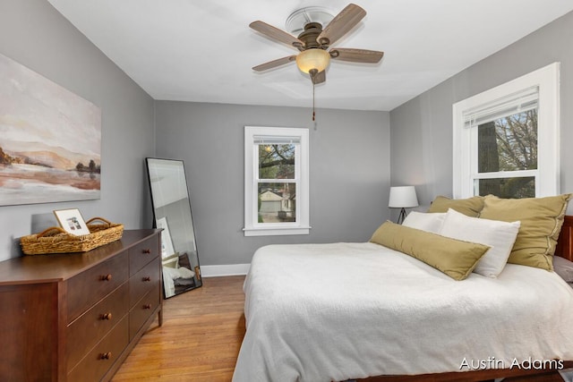 bedroom with baseboards, a ceiling fan, light wood-style flooring, and multiple windows