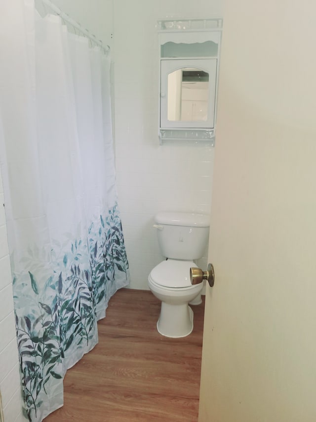 bathroom with tile walls, toilet, wood finished floors, and a shower with shower curtain