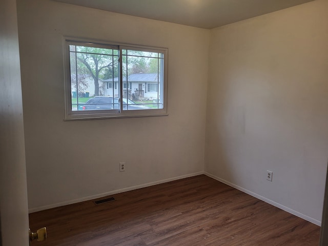 spare room with baseboards, dark wood-style flooring, and visible vents