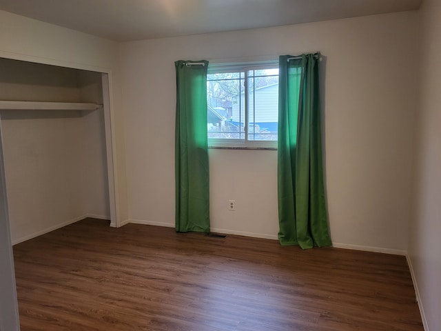unfurnished bedroom with dark wood-style flooring, baseboards, and a closet