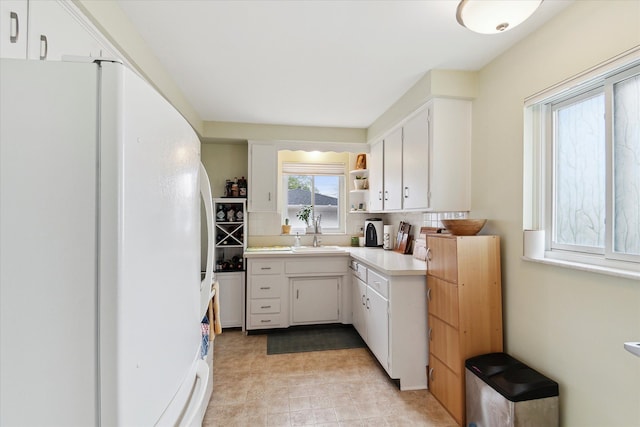kitchen with freestanding refrigerator, light countertops, white cabinetry, and backsplash