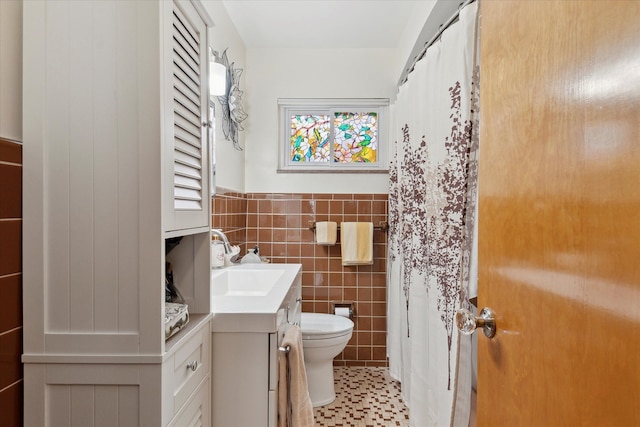 bathroom with wainscoting, vanity, toilet, and tile walls