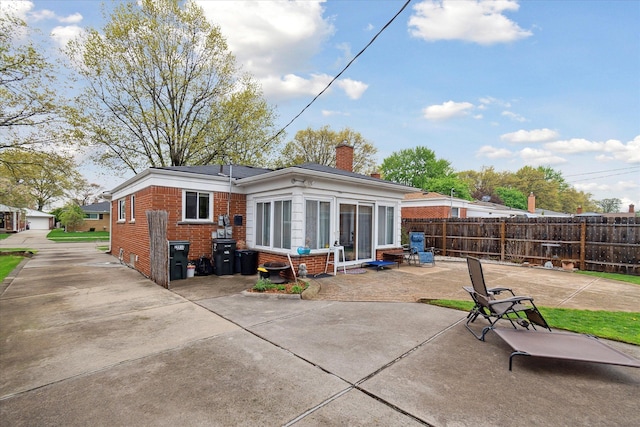back of property featuring brick siding, a chimney, fence, and a patio