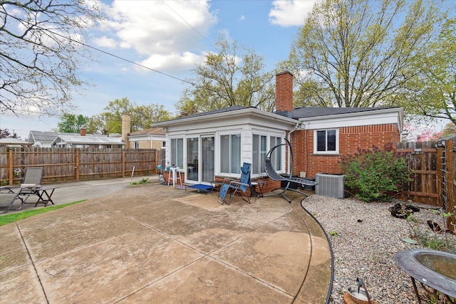 rear view of house featuring brick siding, a patio, a fenced backyard, cooling unit, and a chimney