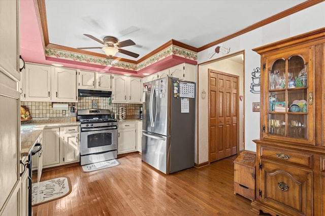 kitchen featuring decorative backsplash, a ceiling fan, appliances with stainless steel finishes, light wood finished floors, and under cabinet range hood