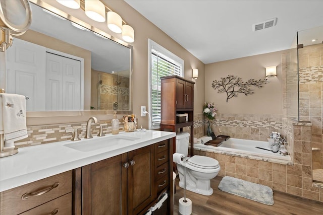 bathroom with a garden tub, visible vents, wood finished floors, vanity, and tiled shower