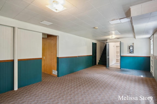 interior space with visible vents, a wainscoted wall, wooden walls, carpet, and stairs