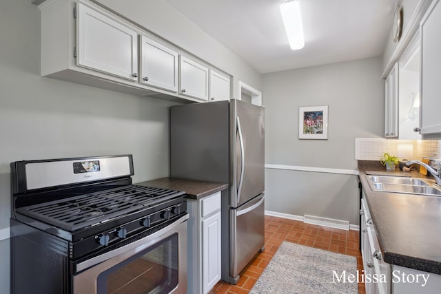 kitchen featuring dark countertops, appliances with stainless steel finishes, a sink, brick floor, and white cabinetry