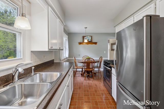 kitchen featuring brick patterned floor, dark countertops, white cabinets, a sink, and appliances with stainless steel finishes