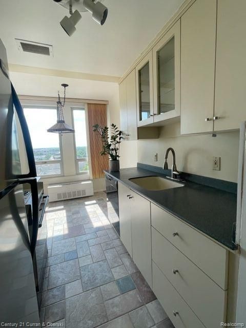 kitchen featuring visible vents, dark countertops, a sink, black appliances, and glass insert cabinets