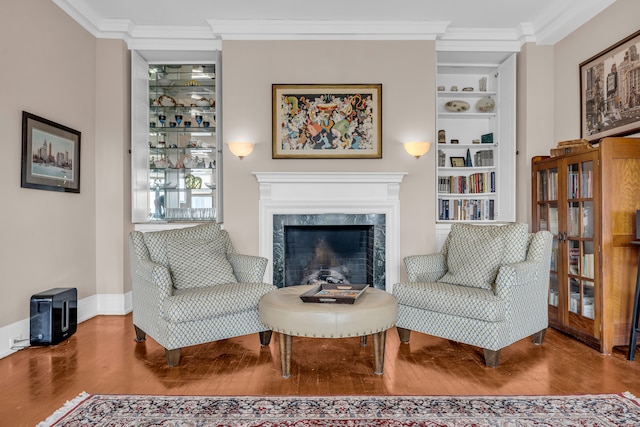living area featuring wood finished floors, crown molding, a premium fireplace, baseboards, and built in features