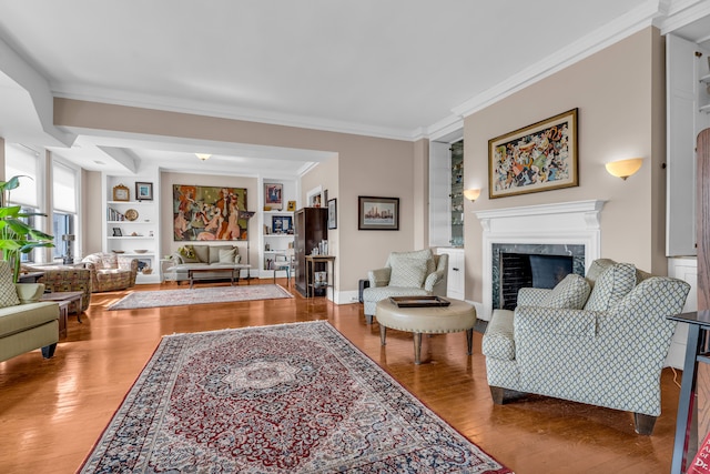 living area featuring built in shelves, wood finished floors, ornamental molding, a high end fireplace, and baseboards