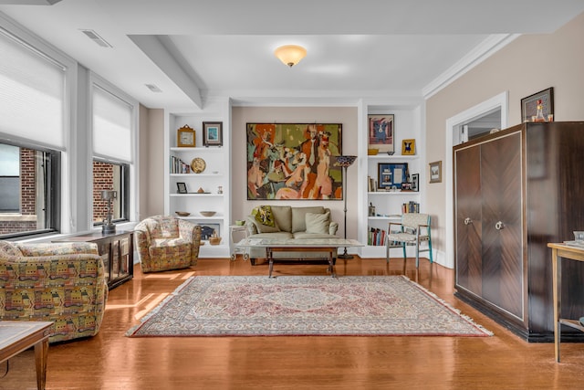 sitting room with wood finished floors, crown molding, and built in features