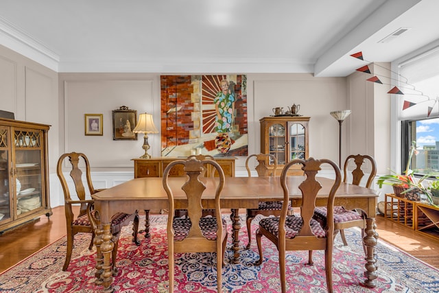 dining area featuring a decorative wall, ornamental molding, and wood finished floors