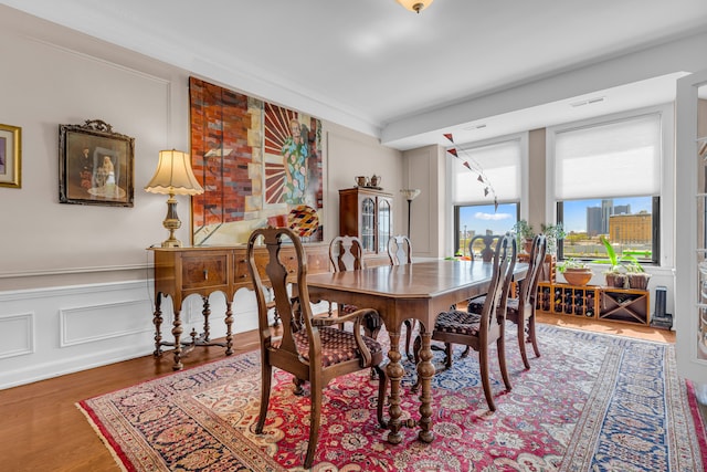 dining space with wood finished floors, a decorative wall, a wainscoted wall, and crown molding