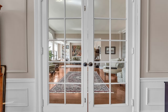 detailed view of ornamental molding, french doors, a decorative wall, wood finished floors, and wainscoting