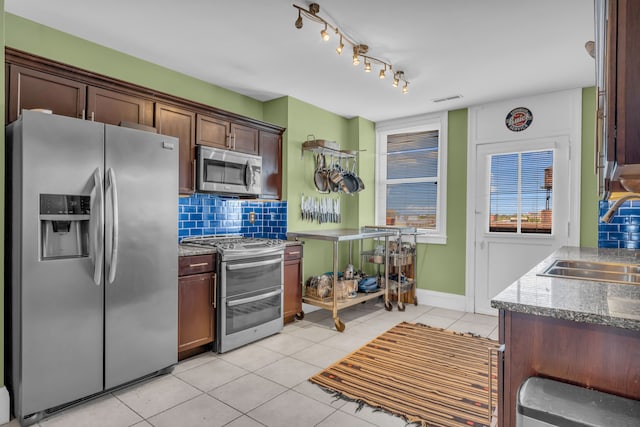 kitchen with appliances with stainless steel finishes, a sink, light tile patterned floors, backsplash, and baseboards