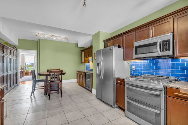 kitchen featuring stainless steel appliances, beverage cooler, rail lighting, decorative backsplash, and light stone countertops