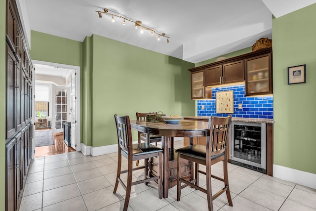 dining space with wine cooler, baseboards, light tile patterned floors, and rail lighting