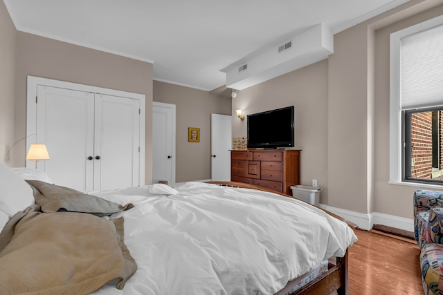 bedroom with light wood-type flooring, baseboards, ornamental molding, and a closet
