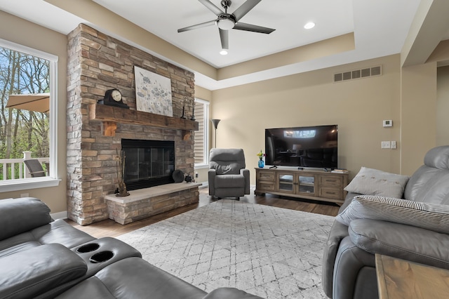 living area with a ceiling fan, visible vents, a fireplace, wood finished floors, and baseboards