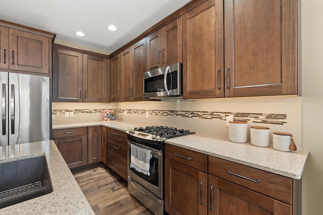 kitchen featuring appliances with stainless steel finishes, wood finished floors, light stone countertops, and tasteful backsplash