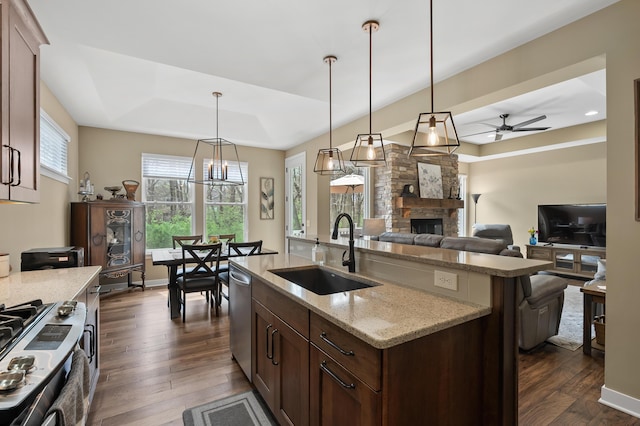 kitchen featuring a sink, a fireplace, stainless steel dishwasher, a tray ceiling, and a center island with sink