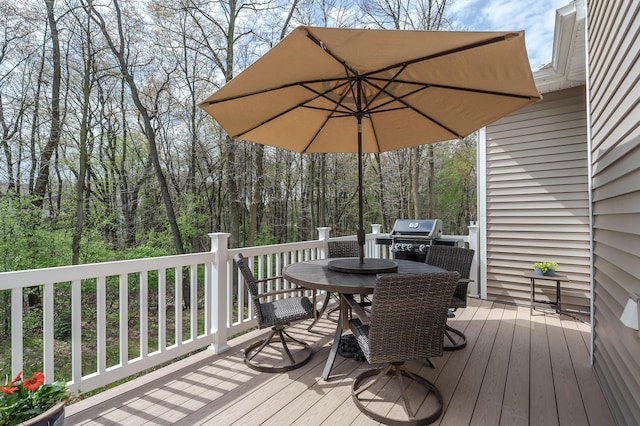 deck with a view of trees, outdoor dining space, and area for grilling