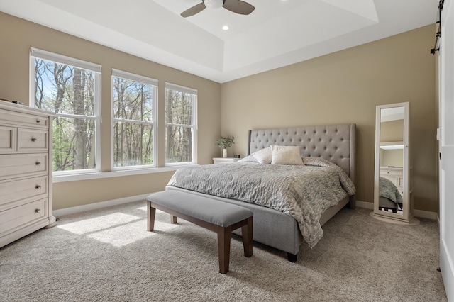 carpeted bedroom featuring a barn door, a ceiling fan, baseboards, recessed lighting, and a tray ceiling