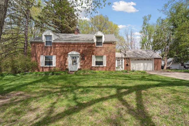 colonial house featuring a front yard, a chimney, brick siding, an attached garage, and driveway