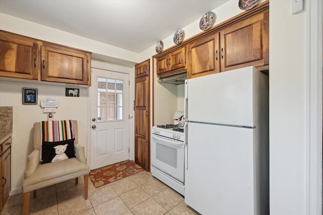 kitchen with light tile patterned floors, under cabinet range hood, brown cabinets, and white appliances