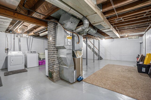 unfinished basement featuring washing machine and clothes dryer, concrete block wall, heating unit, and stairway