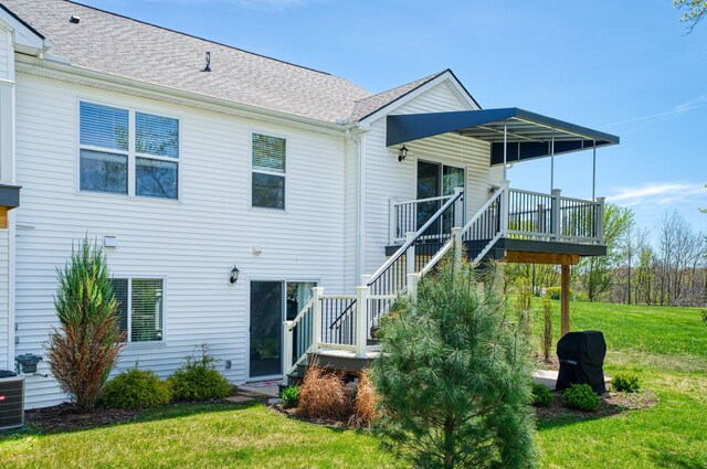 back of property featuring a lawn, a deck, a shingled roof, stairway, and central air condition unit