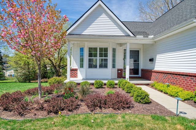 entrance to property featuring a porch, brick siding, and roof with shingles