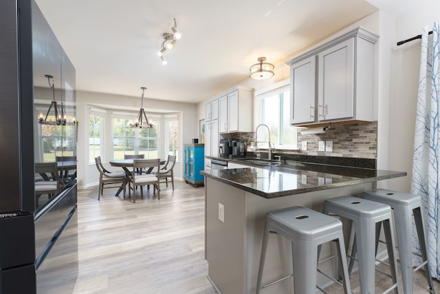 kitchen featuring a sink, freestanding refrigerator, a chandelier, tasteful backsplash, and light wood-type flooring