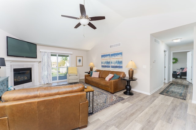 living area featuring ceiling fan, light wood-type flooring, a glass covered fireplace, baseboards, and high vaulted ceiling